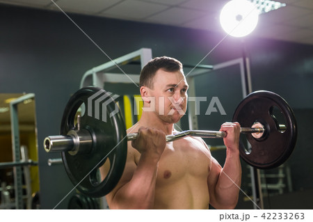 Muscular young man lifting weights in gym 42233263