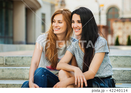 Two girlfriends sitting on the stairs and listening music 42240114