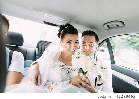 Happy newlywed couple is holding the wedding bouquet of roses while driving in the car. Happy newlywed couple is holding the wedding bouquet of roses while driving in the car. 42259465