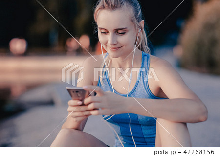 The girl sitting near the water with a smartphone The girl sitting near the water with a smartphone 42268156
