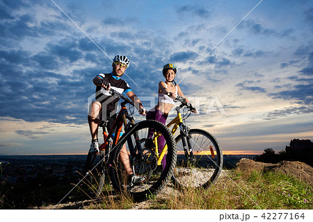 Young people on mountain bikes on top of hill under magic sky at sunset Young people on mountain bikes on top of hill under magic sky at sunset 42277164