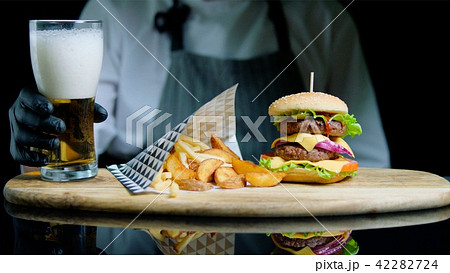 Chef is serving set of tasty burger, french fries and beer on the wooden tray on the black 42282724