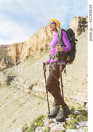 Smiling girl traveler in a yellow hat and a pair of sunglasses stands at the foot of epic rocks with 42290636