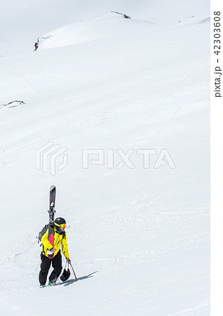 A skier in a helmet and mask with a backpack rises on a slope against the background of snow and a 42303608