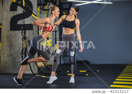 Cheerful girl is using trx straps with instructor Cheerful girl is using trx straps with instructor 42313217
