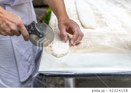 Chef cutting pastry with pizza knife on table top 42324158