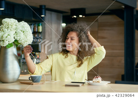 Funny girl with curly hair taking selfie sitting on restaurant's wooden table. Funny girl with curly hair taking selfie sitting on restaurant's wooden table. 42329064