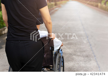 Caretaker walking with patient in wheelchair 42341474