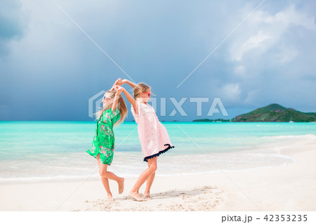 Little happy funny girls have a lot of fun at tropical beach playing together. Sunny day with rain Little happy funny girls have a lot of fun at tropical beach playing together. Sunny day with rain 42353235
