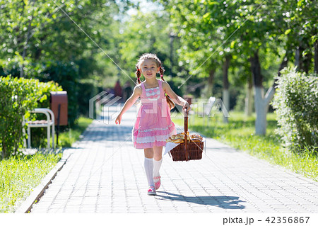 The girl runs along the road with a basket of bread. 42356867