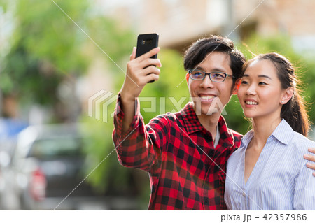 Young happy Asian couple taking selfie together outdoors 42357986