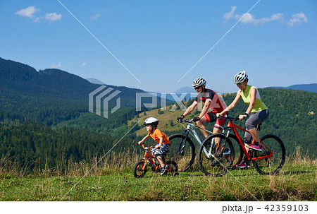 Family tourists bikers, mom, dad and child riding on bicycles on grassy hill 42359103