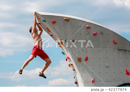 Photo of young sporty brunet in red shorts hanging on wall for rock climbing against blue sky with Photo of young sporty brunet in red shorts hanging on wall for rock climbing against blue sky with 42377974