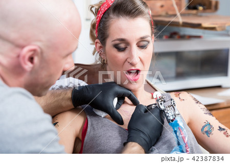 Portrait of a woman getting a painful tattoo on the skin of the chest Portrait of a woman getting a painful tattoo on the skin of the chest 42387834