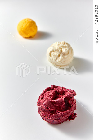 Three balls of delicious natural ice cream - yellow mango, vanilla white, red berry on a white 42392010