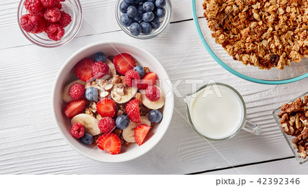 Homemade granola in a plate, sliced banana and strawberries, milk, almonds, blueberries - 42392346