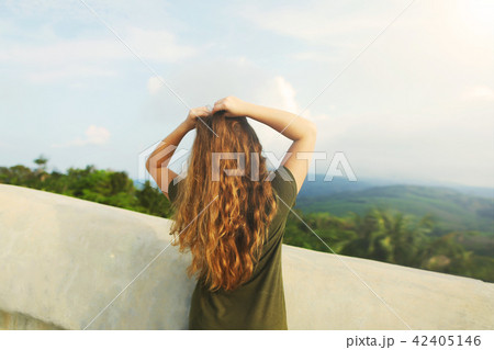Young girl with raised hands wearing khaki dress, standing in mountains background. 42405146