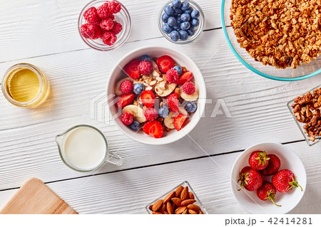 Ingredirnts for preparing healthy organic breakfast - granola, berries honey, milk, banana in white 42414281