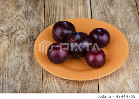 Plums in an orange plate on a wooden table 42444759