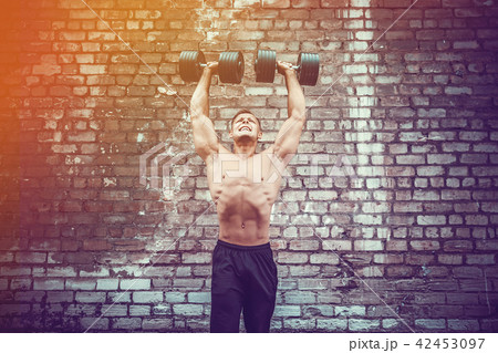 Muscular guy doing exercises with dumbbell against a brick wall 42453097