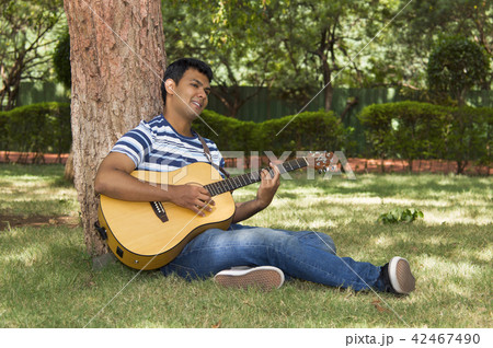 Young man playing guitar under tree 42467490