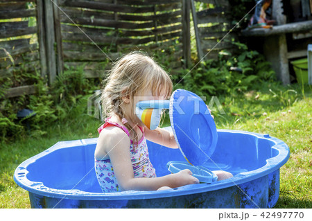 Little girl enjoying a hot summer day while usin her sandpit as swimming pool Little girl enjoying a hot summer day while usin her sandpit as swimming pool 42497770