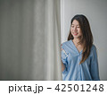 Young asian woman standing beside a window. 42501248