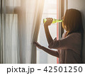 Young asian woman standing beside a window at home 42501250