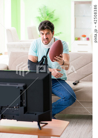 Man with neck and arm injury watching american football on tv Man with neck and arm injury watching american football on tv 42508386