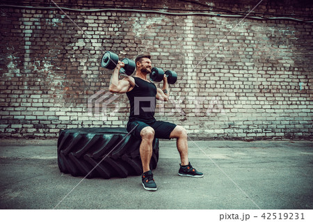 Muscular guy doing exercises with dumbbell against a brick wall 42519231