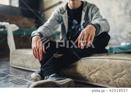 Junkie sitting on the mattress and smoke cigarette 42519557