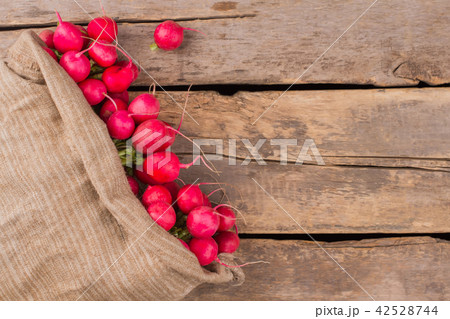 Overfilled sack of radishes on wood. 42528744