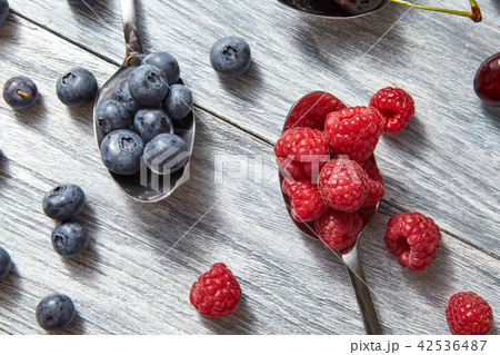 Freshly picked raspberry and blueberry in a spoons on a gray wooden background. Top view. 42536487