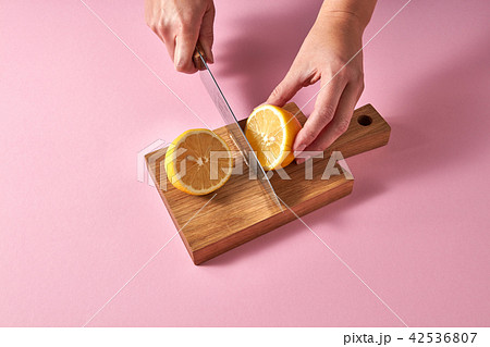 Slices of yellow lemon on a wooden board on a green. Female hands cutting a ripe lemon for preparing 42536807