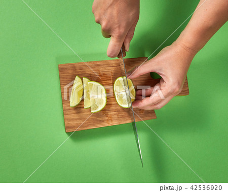 Slices of natural organic green lime, cutting by woman hands on a wooden cutting board on green. 42536920