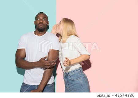 The young couple whispering a secret behind her hand over studio background 42544336