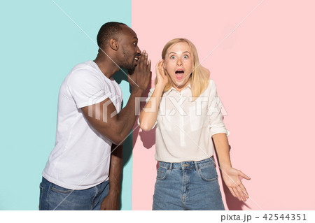The young couple whispering a secret behind her hand over studio background 42544351