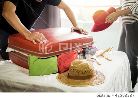 man trying to fit all clothing to packing his red suitcase befor man trying to fit all clothing to packing his red suitcase befor 42563537