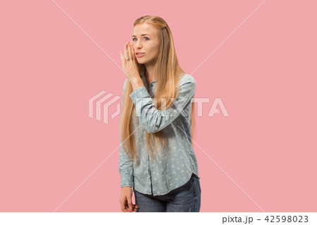The young woman whispering a secret behind her hand over pink background 42598023