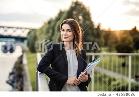 A young businesswoman standing on the river promenade at sunset. A young businesswoman standing on the river promenade at sunset. 42598036