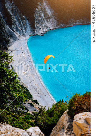 Myrtos Beach, Kefalonia Island, Greece. Figure of a parachutist skydiver with orange parachute 42606607