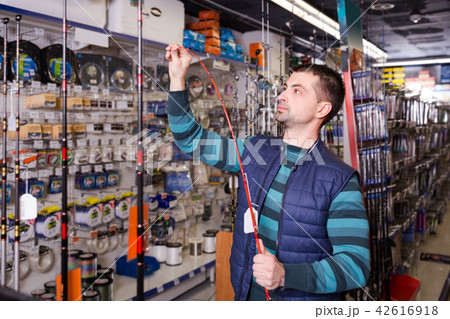 interested male choosing fishing rod for fishing in the sports shop 42616918