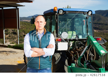 Confident male owner of vineyard posing near tractor outdoors in 42617538