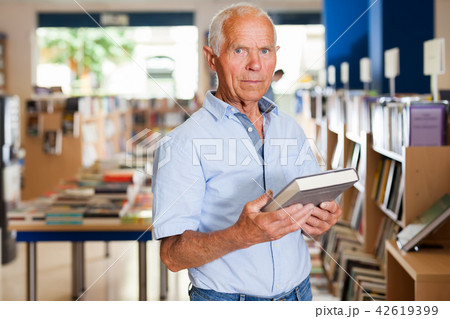 Portrait of intelligent older man in library with book in hands 42619399