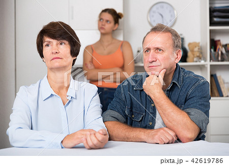 Upset female and her husband are sitting at the table and their daughter is sympathying with them Upset female and her husband are sitting at the table and their daughter is sympathying with them 42619786