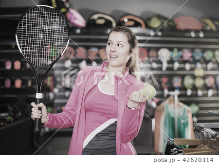 admiring tennis female is choosing new rocket and ball for play in the store 42620314