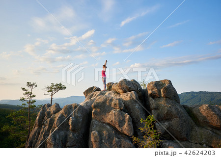 Attractive girl standing with raised hands in yoga pose on top of rocky mountain 42624203