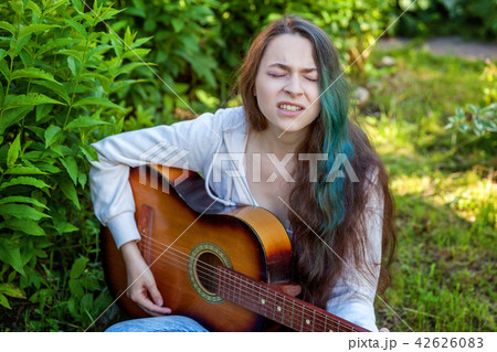 Young woman sitting in grass and playing guitar Young woman sitting in grass and playing guitar 42626083