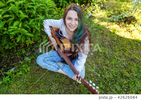Young woman sitting in grass and playing guitar Young woman sitting in grass and playing guitar 42626084