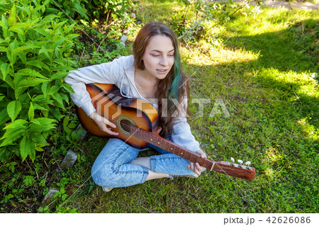 Young woman sitting in grass and playing guitar Young woman sitting in grass and playing guitar 42626086